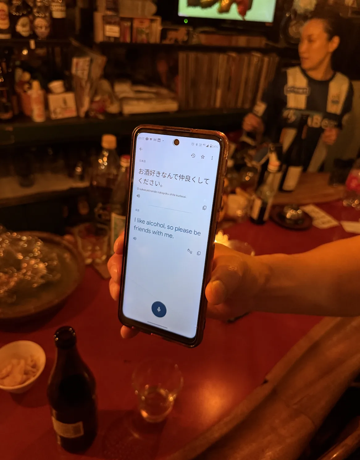 A small Tokyo bar at night, phone translation open between strangers